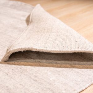 A woven light beige rug is folded back on light wood flooring, revealing striped backing detail.