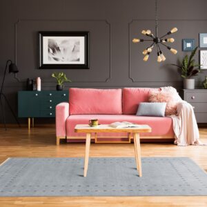 Light blue rug with a minimalist geometric border pattern centers a living room with a pink sofa.