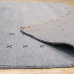 Pale blue rug with dark cross patterns is displayed folded back over light wood floor.