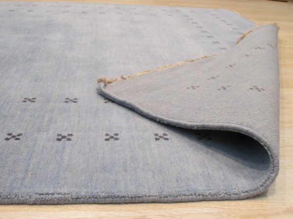 Pale blue rug with dark cross patterns is displayed folded back over light wood floor.