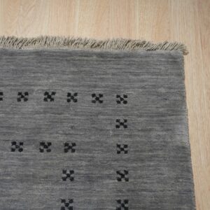 Grey textured rug featuring repeating black geometric crosses and light fringe on wooden planks.