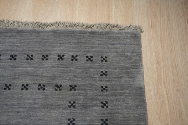 Grey textured rug featuring repeating black geometric crosses and light fringe on wooden planks.