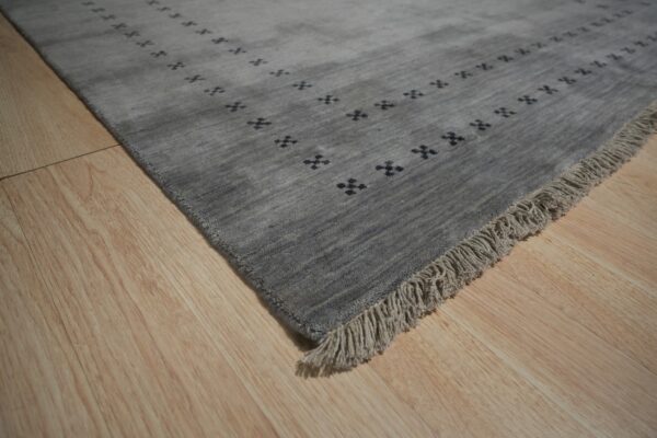 Textured gray rug with dark cross motifs and matching fringe rests on light blonde wood plank flooring.