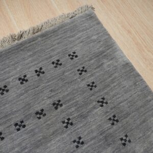 A gray, textured rug with black geometric symbols rests on light wood flooring and features fringe.