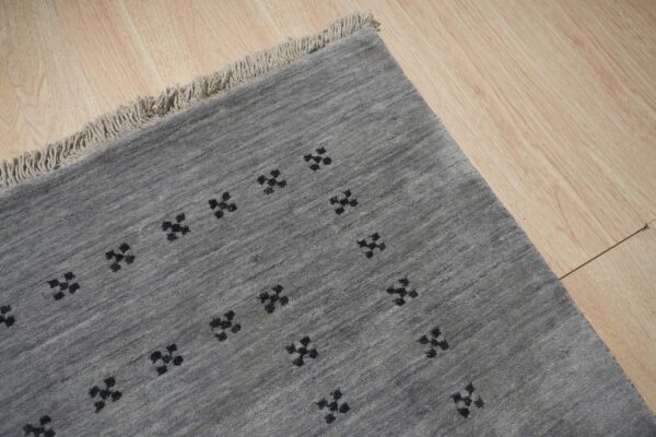 A gray, textured rug with black geometric symbols rests on light wood flooring and features fringe.