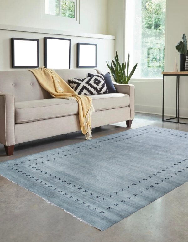 Light blue textured rug with a subtle dark geometric border on concrete next to a neutral sofa.