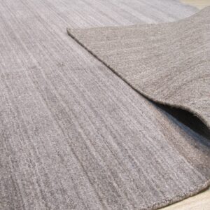 Low-pile beige rug with subtle texture folded to show the backing on light wood floors.