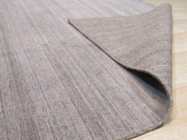 Low-pile beige rug with subtle texture folded to show the backing on light wood floors.