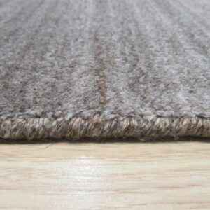 Textured grey and taupe rug edge with thick binding rests on glossy light wood flooring.