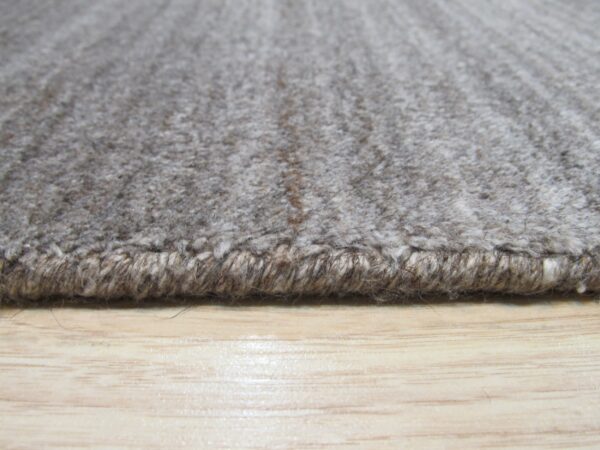 Textured grey and taupe rug edge with thick binding rests on glossy light wood flooring.
