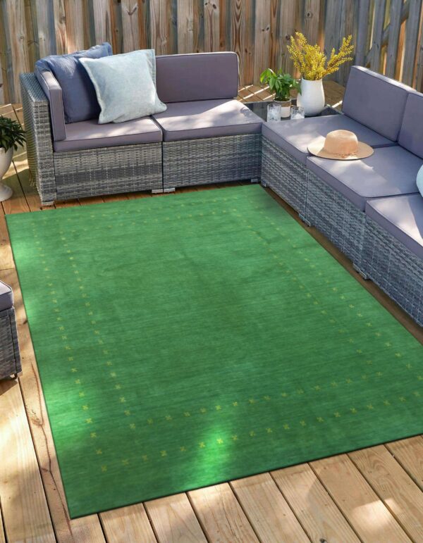 A bright green rug with a subtle yellow border pattern lies on a wooden deck next to a gray sofa.