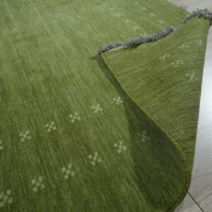 Olive green textured rug with faint white patterns and gray fringes rests on pale wood floorboards.