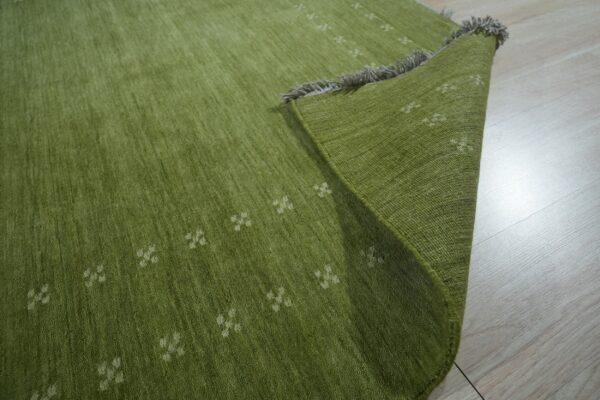 Olive green textured rug with faint white patterns and gray fringes rests on pale wood floorboards.