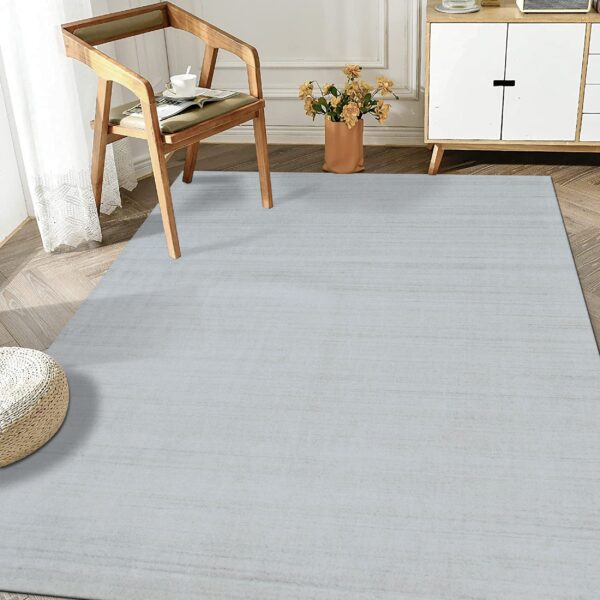 Streaked pale blue-gray area rug covers herringbone wood flooring near a wooden chair and white cabinet.
