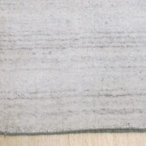 A close-up of a light gray rug with subtle dark horizontal stripes on light wood floorboards.