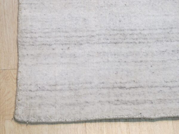 A close-up of a light gray rug with subtle dark horizontal stripes on light wood floorboards.