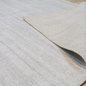 A light gray rug is curled back, showing its tightly woven beige backing on light wood floors.