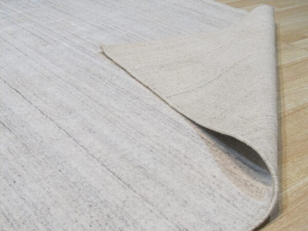 A light gray rug is curled back, showing its tightly woven beige backing on light wood floors.