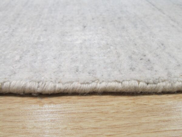 Textured gray and cream rug edge with visible binding rests on a shiny light wood floor.