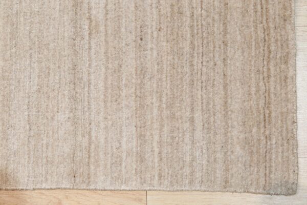 Beige high-pile rug featuring slight vertical striping rests on light wood plank flooring.