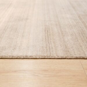 Low-angle view of a textured light beige area rug with a low pile on blonde wood-look flooring.
