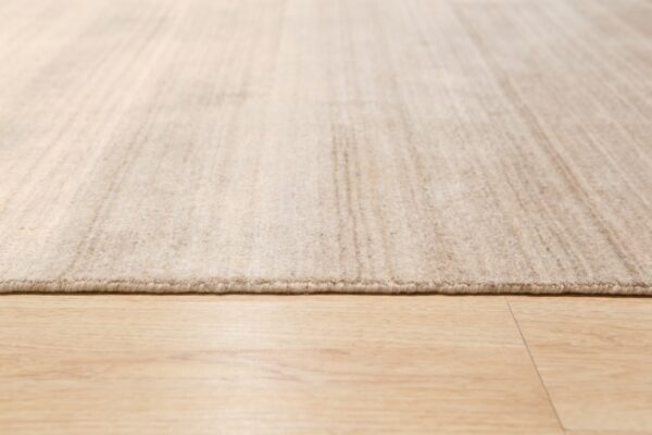 Low-angle view of a textured light beige area rug with a low pile on blonde wood-look flooring.