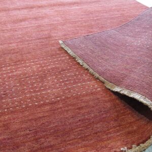 Reddish-orange low-pile rug with scattered white dots is rolled back, showing a woven backing on light flooring.