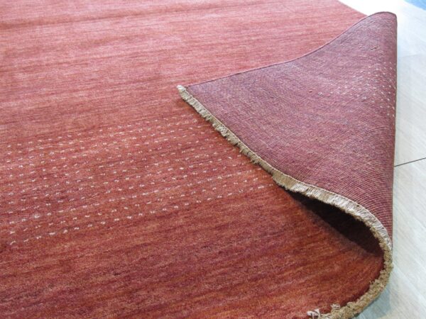 Reddish-orange low-pile rug with scattered white dots is rolled back, showing a woven backing on light flooring.