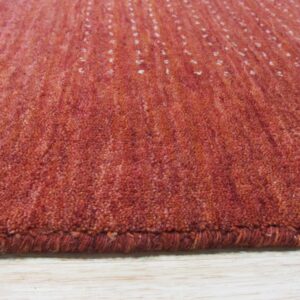 Side view of a dense, rust-colored rug featuring subtle stripe texture on light wood grain.