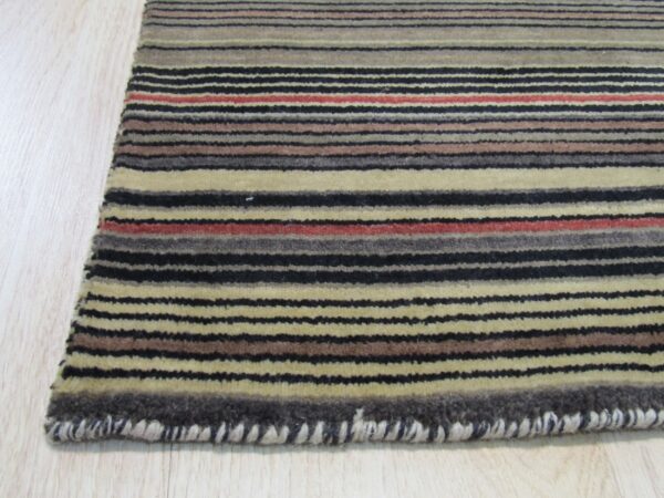 Rug detail showing multicolored horizontal stripes in black, beige, brown, and red on pale wood flooring.