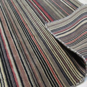 Low pile rug featuring multi-colored vertical stripes is partially rolled on light wood floor.