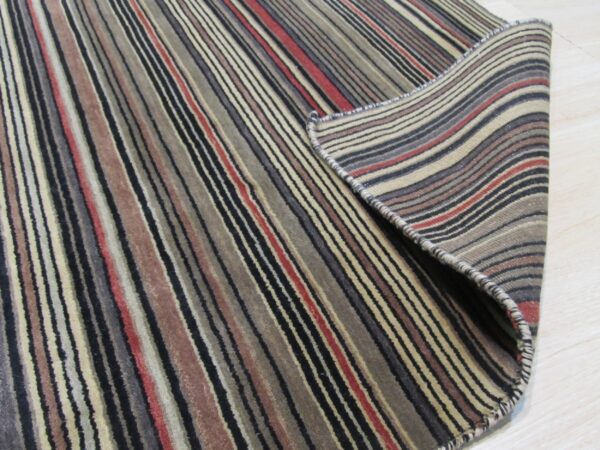 Low pile rug featuring multi-colored vertical stripes is partially rolled on light wood floor.