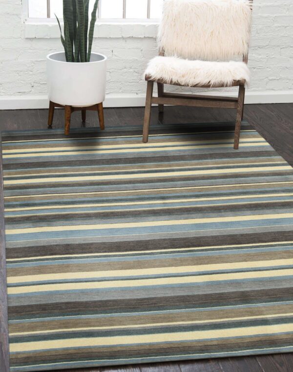 Blue, gray, taupe, and cream striped rug on dark hardwood next to a plant and a fuzzy chair.