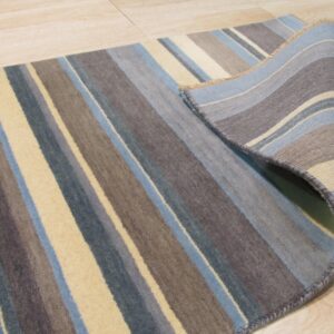 Multicolored striped rug in blue, gray, and tan is shown partially rolled on light wood flooring.