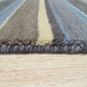 Close up of a striped rug edge with blue, gray, and cream medium pile on a light wood floor.