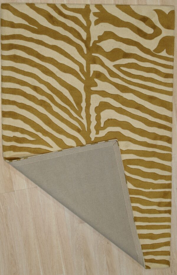 Gold and cream zebra-striped rug on light wood flooring with one corner folded, showing the backing.