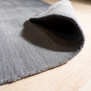 The edge of a solid gray low-pile rug is curled back, resting on pale hardwood floors.