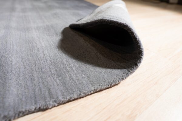 The edge of a solid gray low-pile rug is curled back, resting on pale hardwood floors.