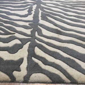 Perspective view of a gray and cream carved zebra pattern rug resting on a light wood floor.