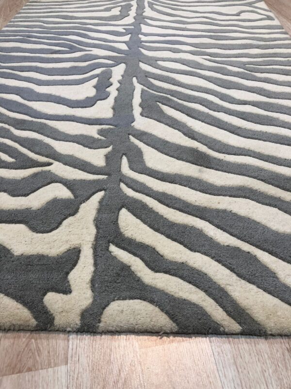 Perspective view of a gray and cream carved zebra pattern rug resting on a light wood floor.