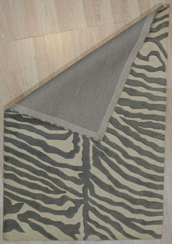 Gray and cream striped rug on light wood floor, corner folded back to show gray backing.