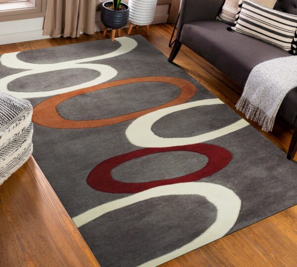 Gray rug with abstract white, rust, and red loops on wood flooring near a dark couch.