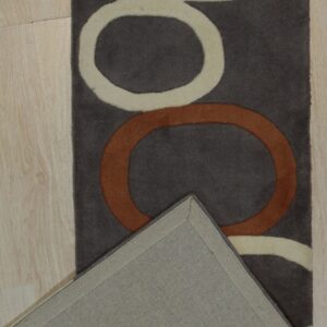 Dark brown rug featuring cream and rust interlocking loops, folded back to reveal the woven backing on wood floor.