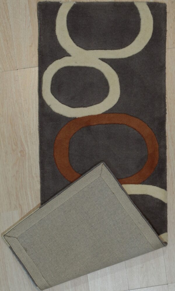 Dark brown rug featuring cream and rust interlocking loops, folded back to reveal the woven backing on wood floor.