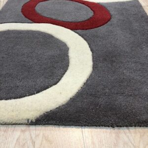 Close-up of a textured gray rug with carved red and cream curved designs on light wood plank flooring.
