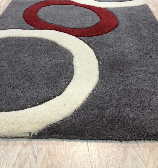 Close-up of a textured gray rug with carved red and cream curved designs on light wood plank flooring.