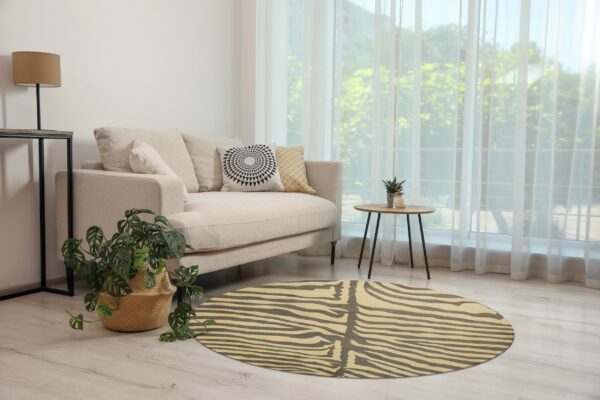 A round rug with a cream and dark gray striped animal print pattern is on light wood flooring.