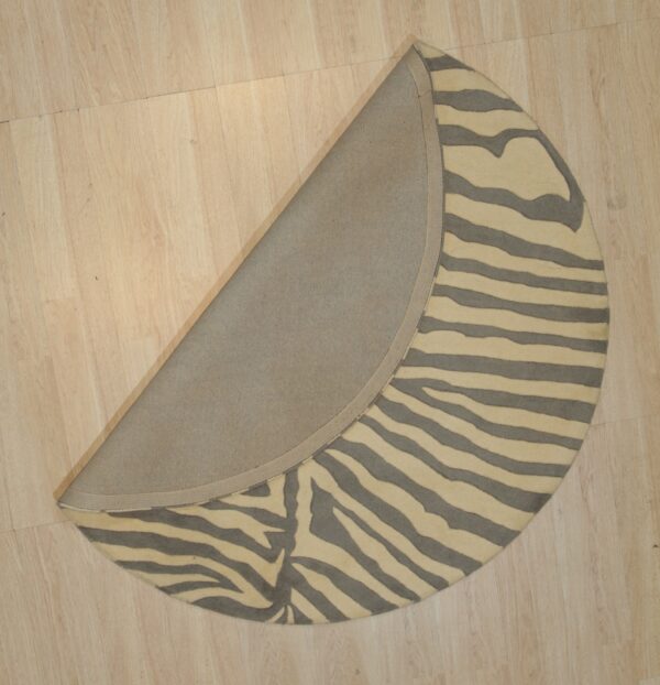 Round zebra-striped rug, cream and gray, folded to reveal the fabric backing on a light wood floor.