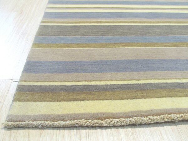 A striped rug with muted blue, gray, gold, and cream colors lies on light plank flooring.
