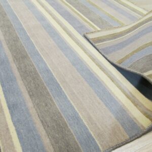 Close-up of a striped blue, taupe, and cream rug rolled back on a light wood floor.